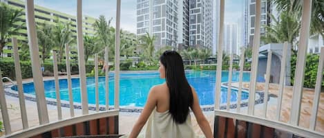 A person sitting by a pool with a view of high-rise buildings and palm trees.
