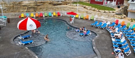 A swimming pool area with multiple lanes, lounge chairs, and umbrellas.