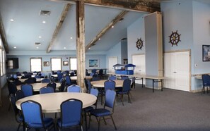 Une salle de conférence dotée de plusieurs tables et chaises, de poutres en bois au plafond et de décorations murales sur le thème de la marine.