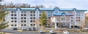 A multi-story hotel with a blue roof, parking lot, and several trees.