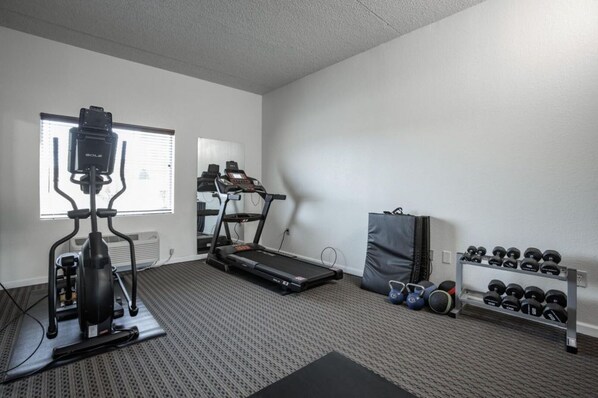 A gym with an elliptical, treadmill, and a rack of dumbbells.