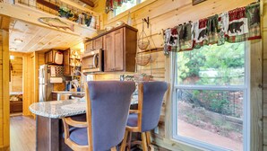 L’intérieur d’un chalet en bois comprend un coin cuisine, deux tabourets de bar et une grande fenêtre donnant sur l’extérieur.