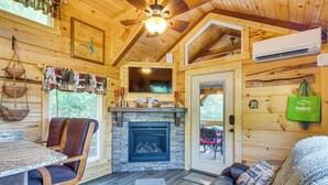 L’intérieur chaleureux d’un chalet avec une cheminée en pierre, des murs en bois, un ventilateur de plafond et un coin repas comprenant une table et des chaises.