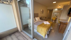 A modern hotel room with a sliding glass door leading to a balcony, a bed with a yellow blanket, a small sofa, and a dining area with yellow chairs. - Luxurious Studio In San Telmo Paseo De La Cisterna (Buenos Aires)