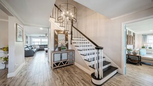 A modern staircase with a wooden finish and black railings, leading to a living area with a gray sofa and a decorative mirror. - Beautiful Water Front home in Port St Lucie FL (Port St. Lucie)