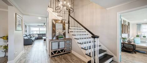 A modern staircase with a wooden finish and black railings, leading to a living area with a gray sofa and a decorative mirror.