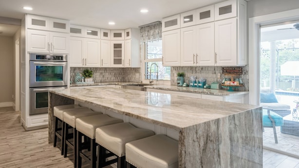 A modern kitchen with white cabinets, a large marble island with bar stools, stainless steel appliances, and a view to the outdoors. - Beautiful Water Front home in Port St Lucie FL (Port St. Lucie)