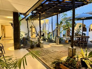 Un vaste espace extérieur agrémenté d’une pergola, de plantes en pot et d’un coin salon avec des chaises et des tables en bois.