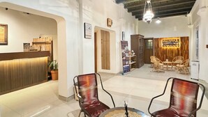 A hotel reception area with a reception desk, a clock, and a reception sign. There are two wicker chairs and a small table with a decorative item. - The Raden Patah Heritage Kota Lama (Semarang)