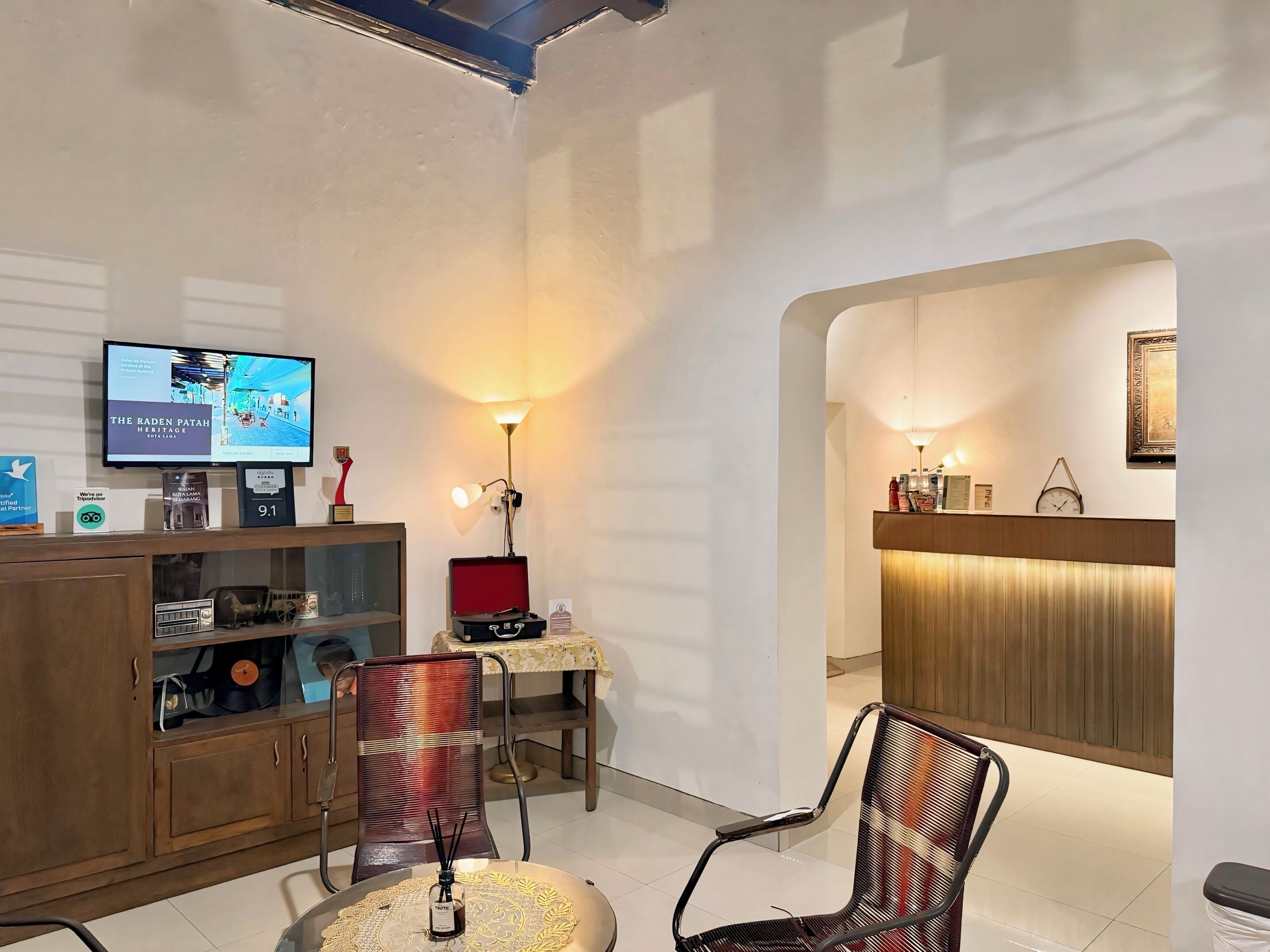 Ein modernes Hotelzimmer mit Fernseher, einem roten Koffer, einer Lampe und einer Sitzecke mit zwei Sesseln.