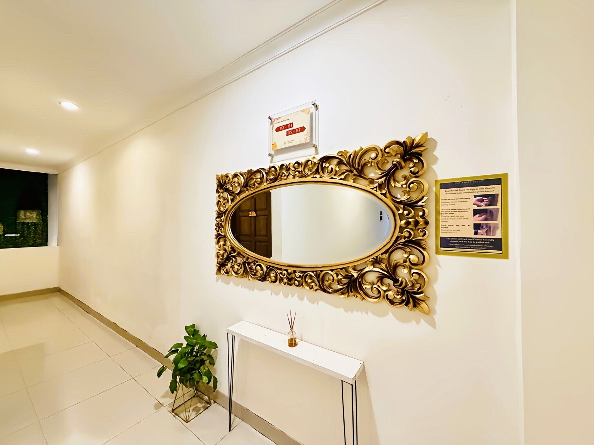 A hallway with a large ornate mirror on the wall, a white console table, and a potted plant.
