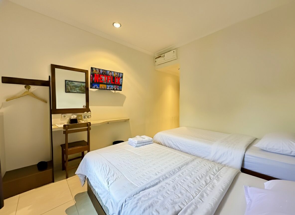 A hotel room with two beds, a mirror, a TV, and a small desk with a chair.