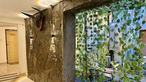 A lobby with a stone wall, a ceiling fan, and a view of a garden with hanging plants. - The Raden Patah Heritage Kota Lama (Semarang)