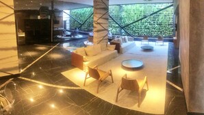 Un hall d’entrée spacieux avec un sol en marbre, un coin salon doté de canapés et de fauteuils, et une grande fenêtre offrant une vue sur la verdure.