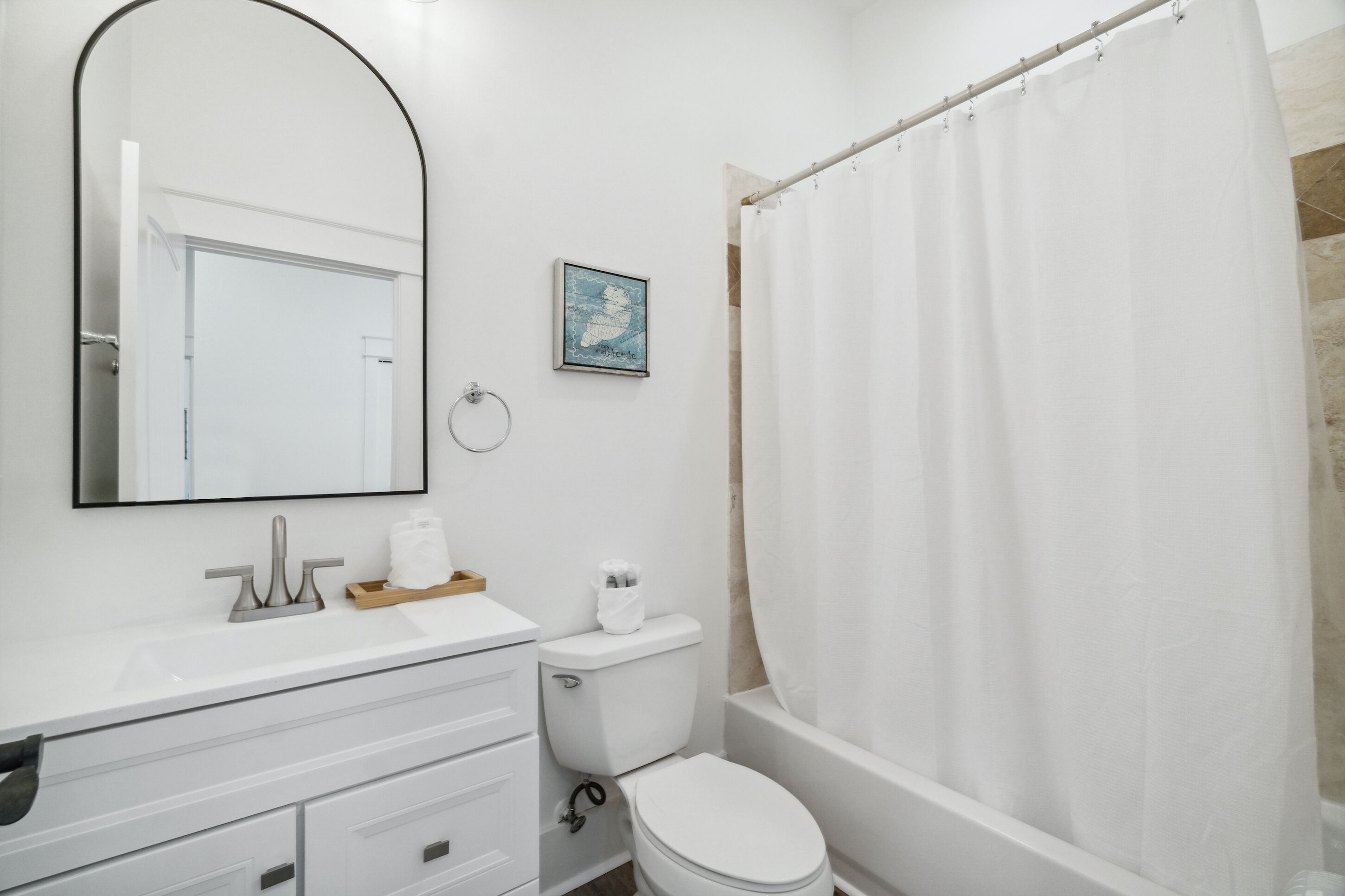 A bathroom with a white sink, mirror, toilet, and shower curtain.