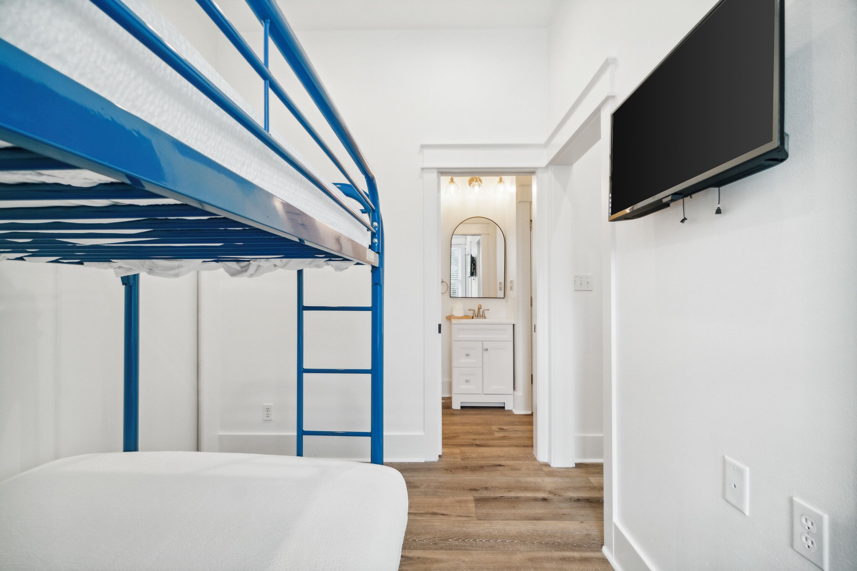 A bedroom with a bunk bed, a TV mounted on the wall, and a bathroom visible through an open door.