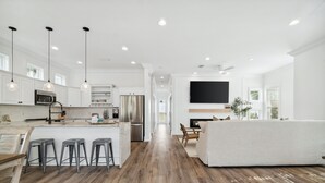 Una cocina moderna con armarios blancos, electrodomésticos de acero inoxidable y una isla central con taburetes.