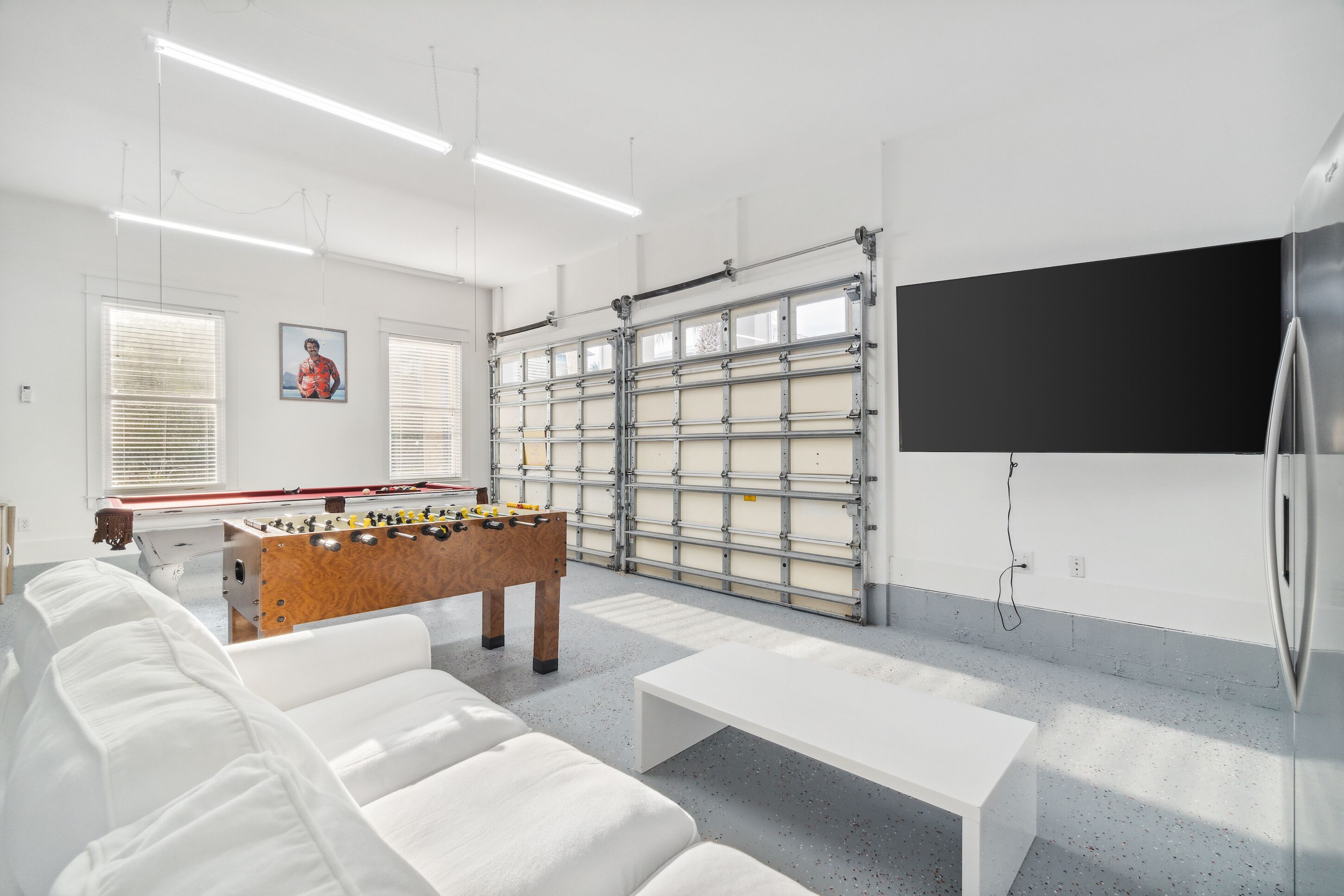 Ein modernes Zimmer mit einem Kicker, einem weißen Sofa, einem weißen Tisch und einem großen an der Wand befestigten Fernsehbildschirm.