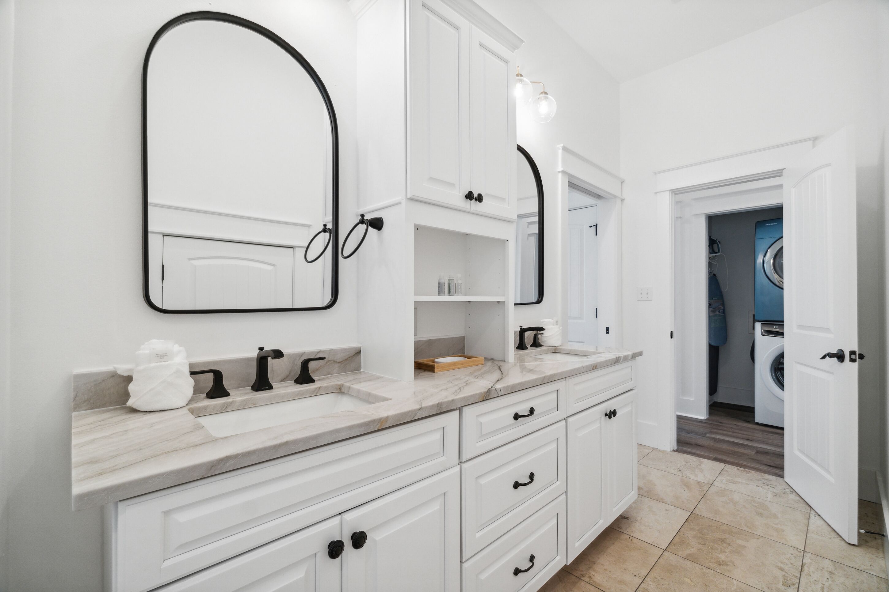 A modern bathroom with white cabinetry, a marble countertop, and a built-in washing machine.