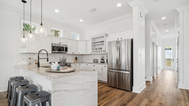 Una cocina moderna con muebles blancos, una isla grande, electrodomésticos de acero inoxidable y suelo de madera.