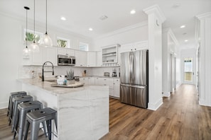 Une cuisine moderne avec des meubles blancs, un grand îlot central, des appareils en acier inoxydable et un revêtement de sol en bois.