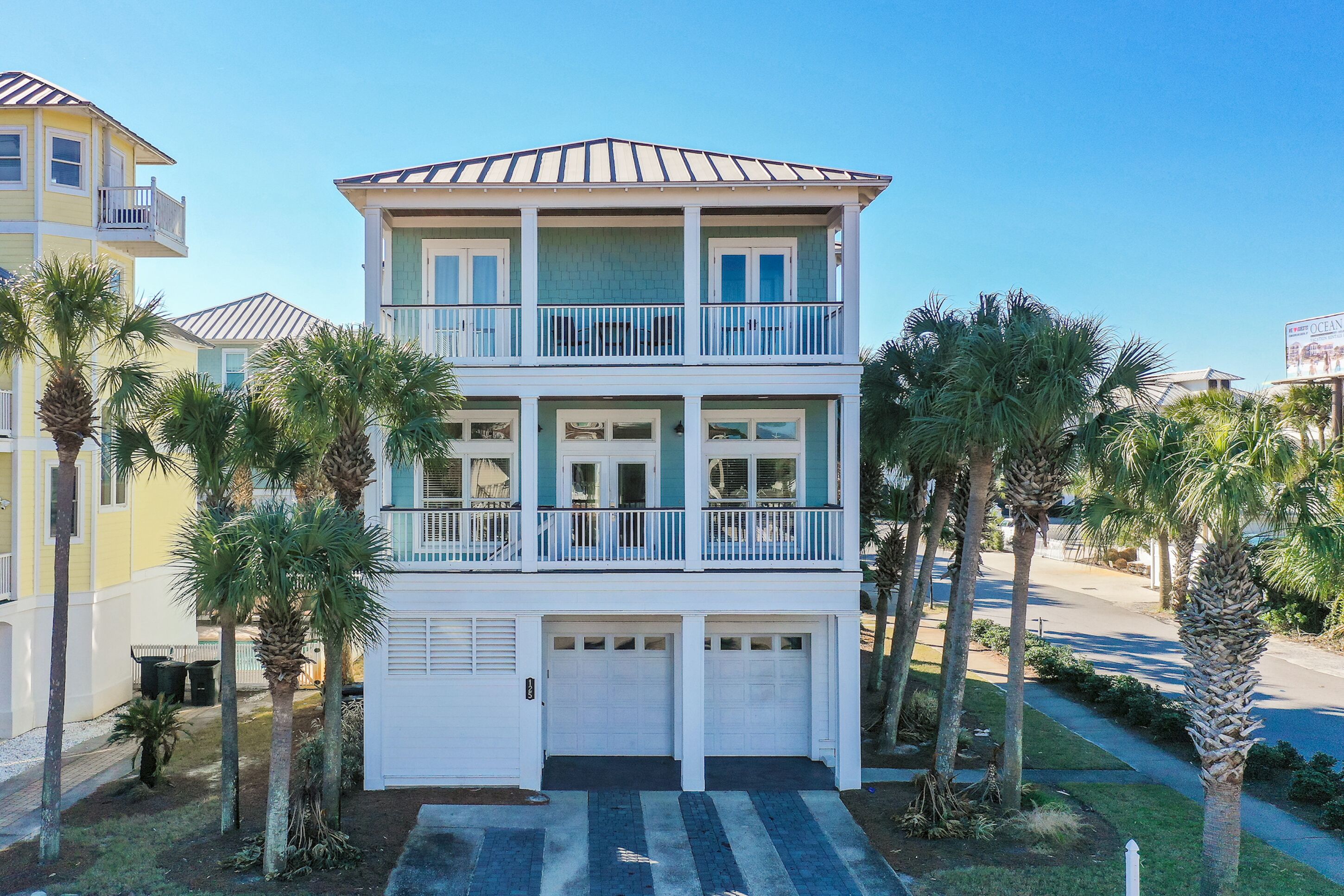 A multi-story residential building with a balcony, garage, and palm trees.