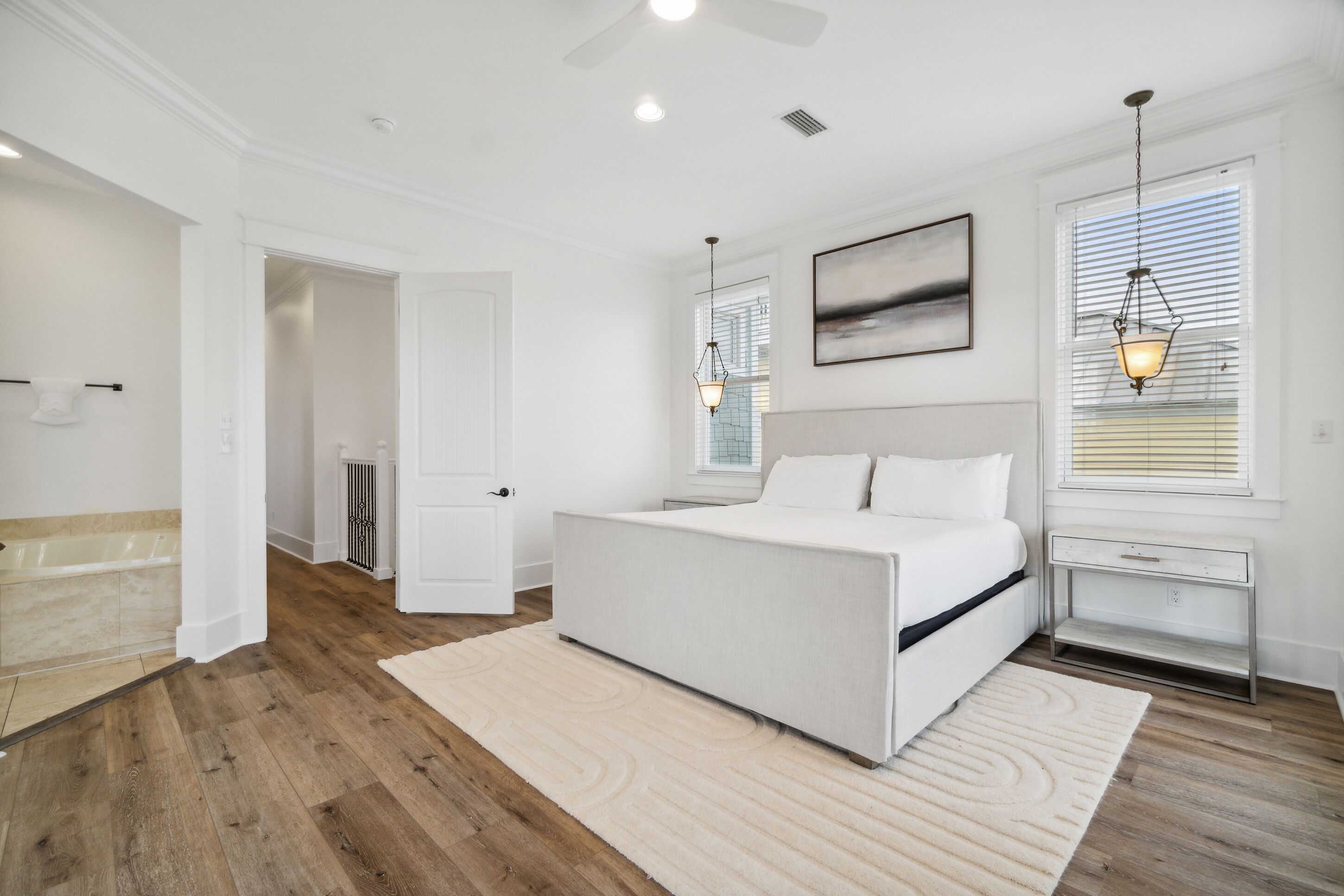 A bedroom with a large bed, a nightstand, a window with blinds, and a ceiling fan.