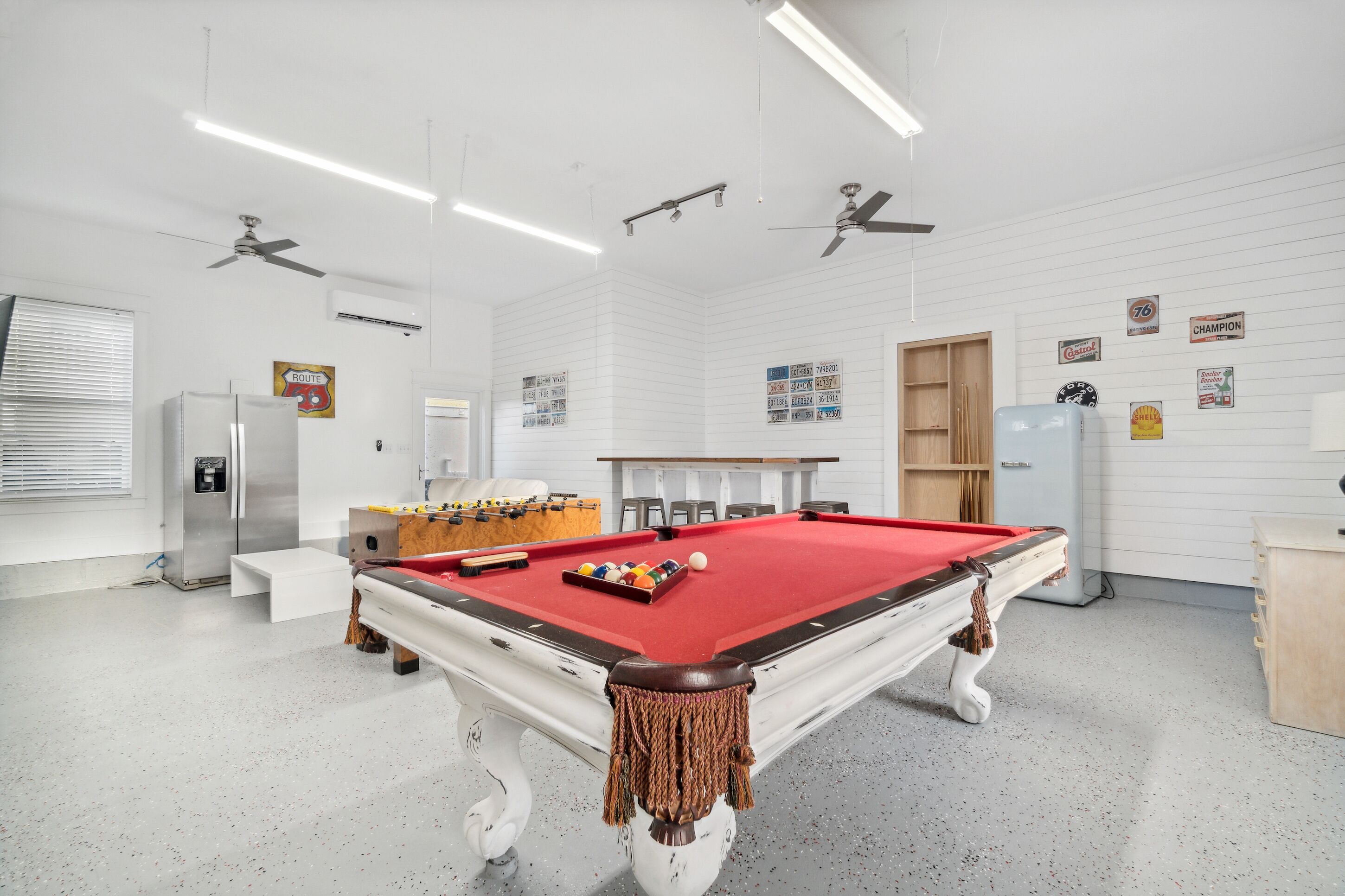 Une table de billard recouverte d’un feutre rouge, une table de baby-foot et un réfrigérateur.