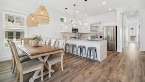 Una cocina moderna con armarios blancos, una isla central con taburetes y luminarias colgantes.