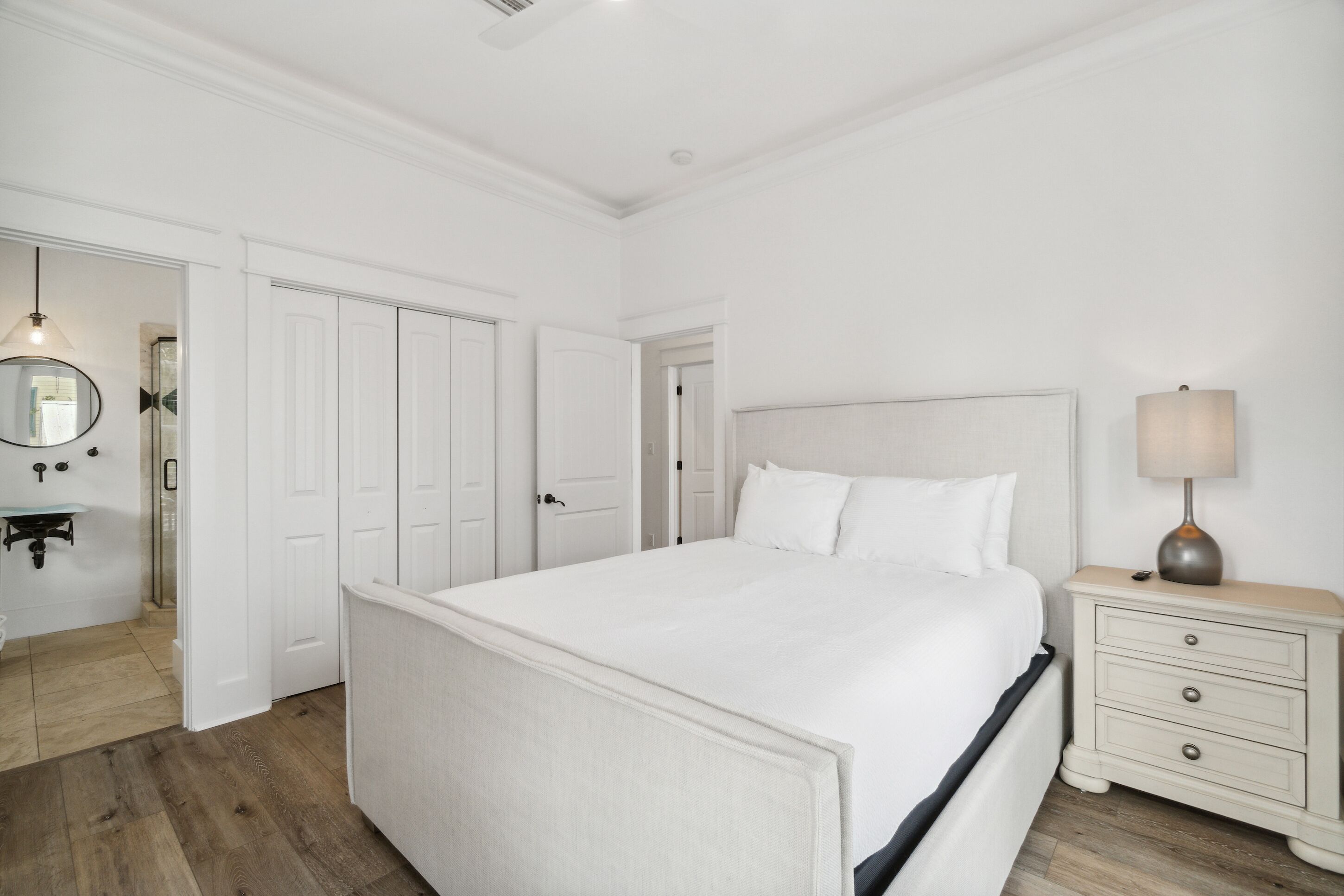 Un dormitorio amplio con una cama grande, una mesita de noche con lámpara y un espejo en la pared.