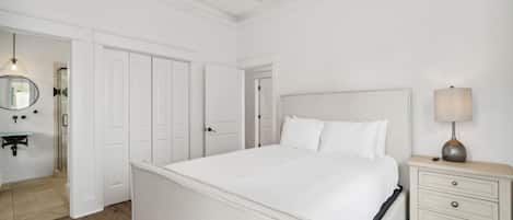 Un dormitorio amplio con una cama grande, una mesita de noche con lámpara y un espejo en la pared.