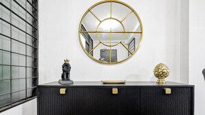 Une console noire avec des poignées dorées, un miroir encadré d’or et deux objets décoratifs posés sur le dessus.