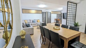 Un salon moderne avec une grande table à manger en bois, des chaises noires et un canapé gris agrémenté de coussins jaunes.