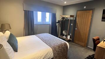 Une chambre d’hôtel comprenant un lit, un bureau, une chaise, un miroir, une armoire et une fenêtre avec des rideaux.