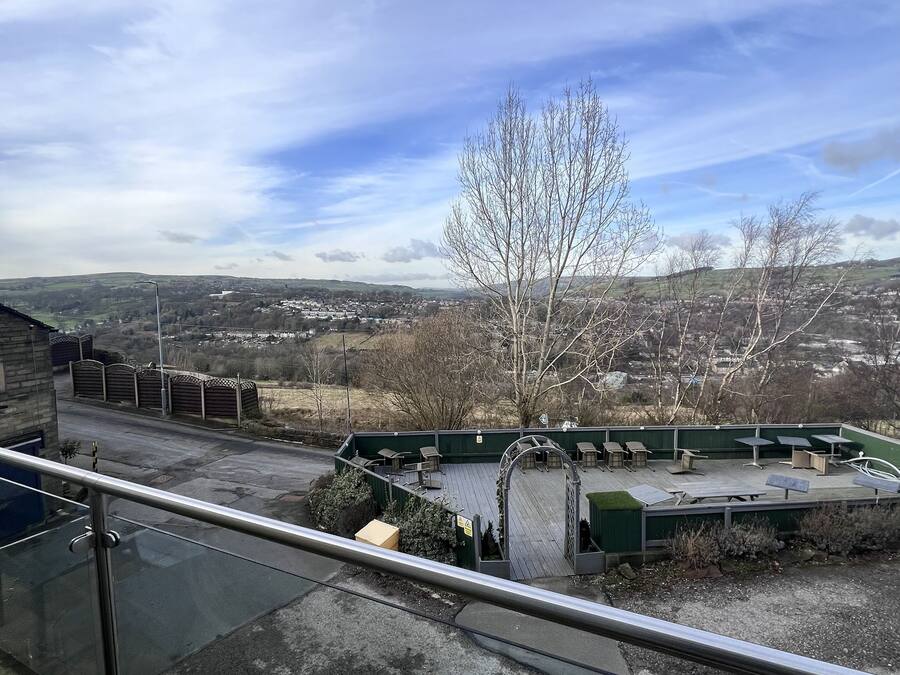 Vista de uma varanda com vista para uma área verde externa, com assentos e uma árvore.