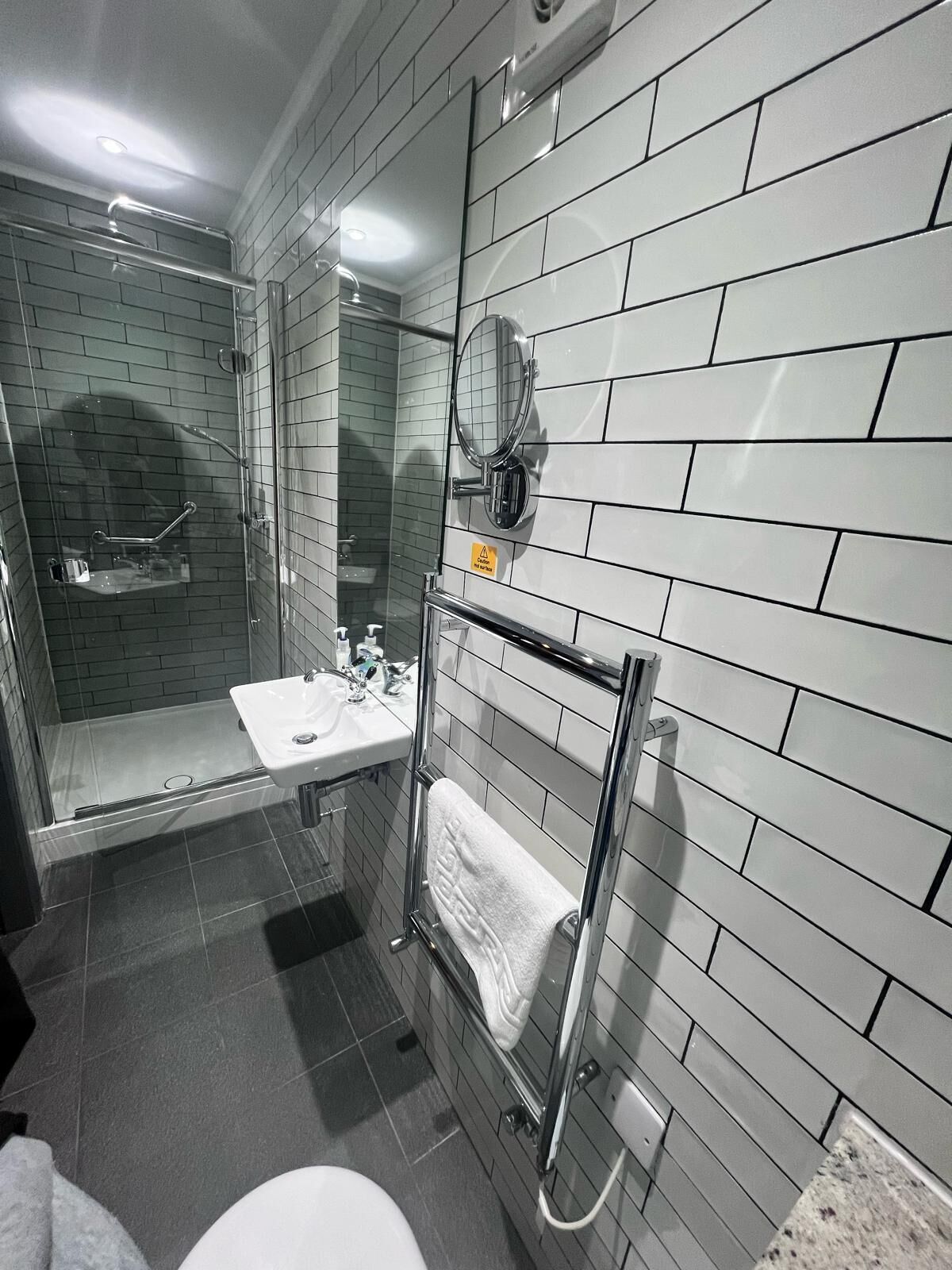 A modern bathroom with a glass shower enclosure, a white sink, and a towel rack.