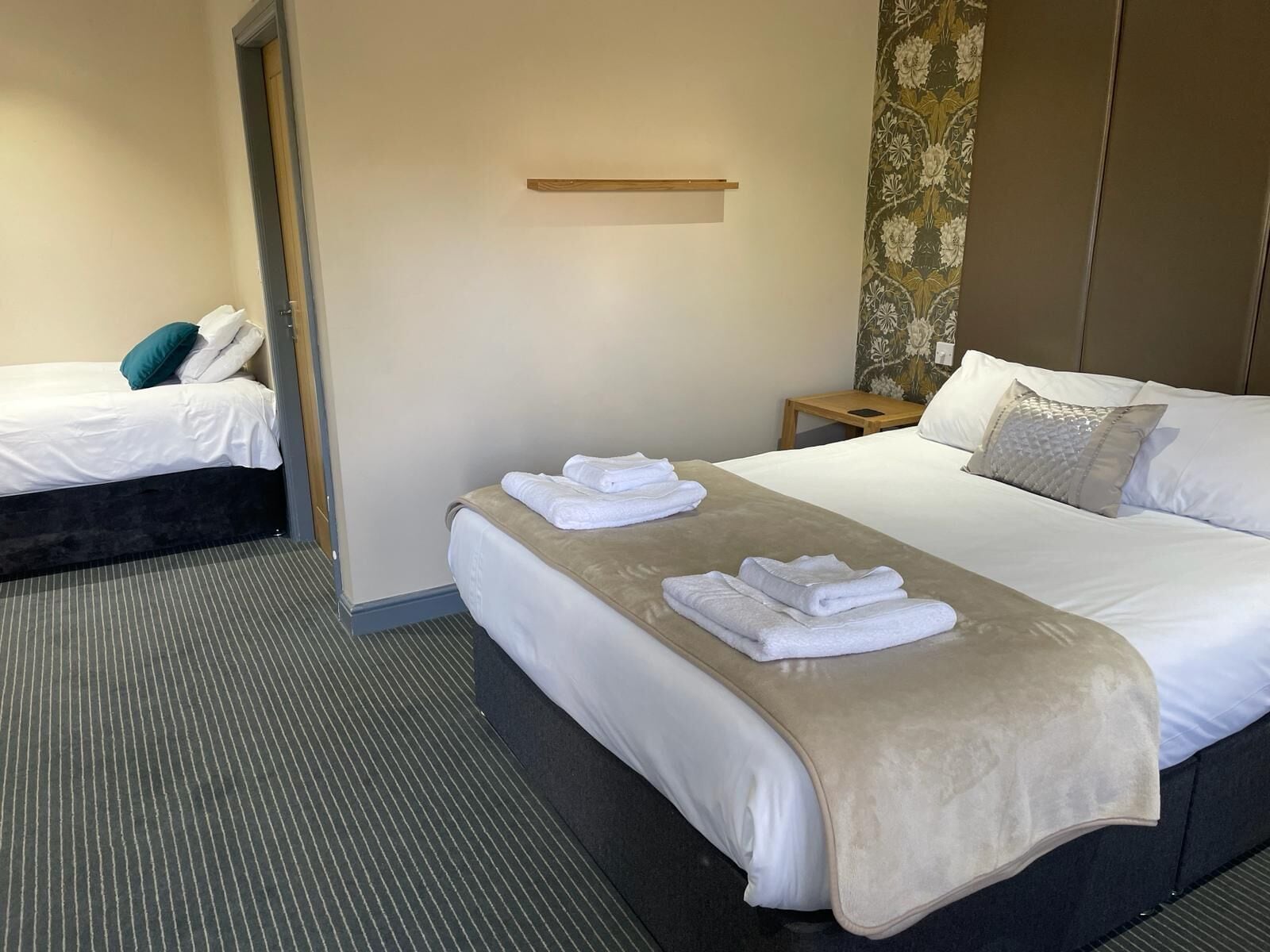 Habitación de hotel con dos camas, una mesita de noche y un estante en la pared.