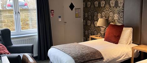 Une chambre d’hôtel avec un lit, deux tables de chevet, un bureau, une chaise et une fenêtre donnant sur une voiture garée à l’extérieur.