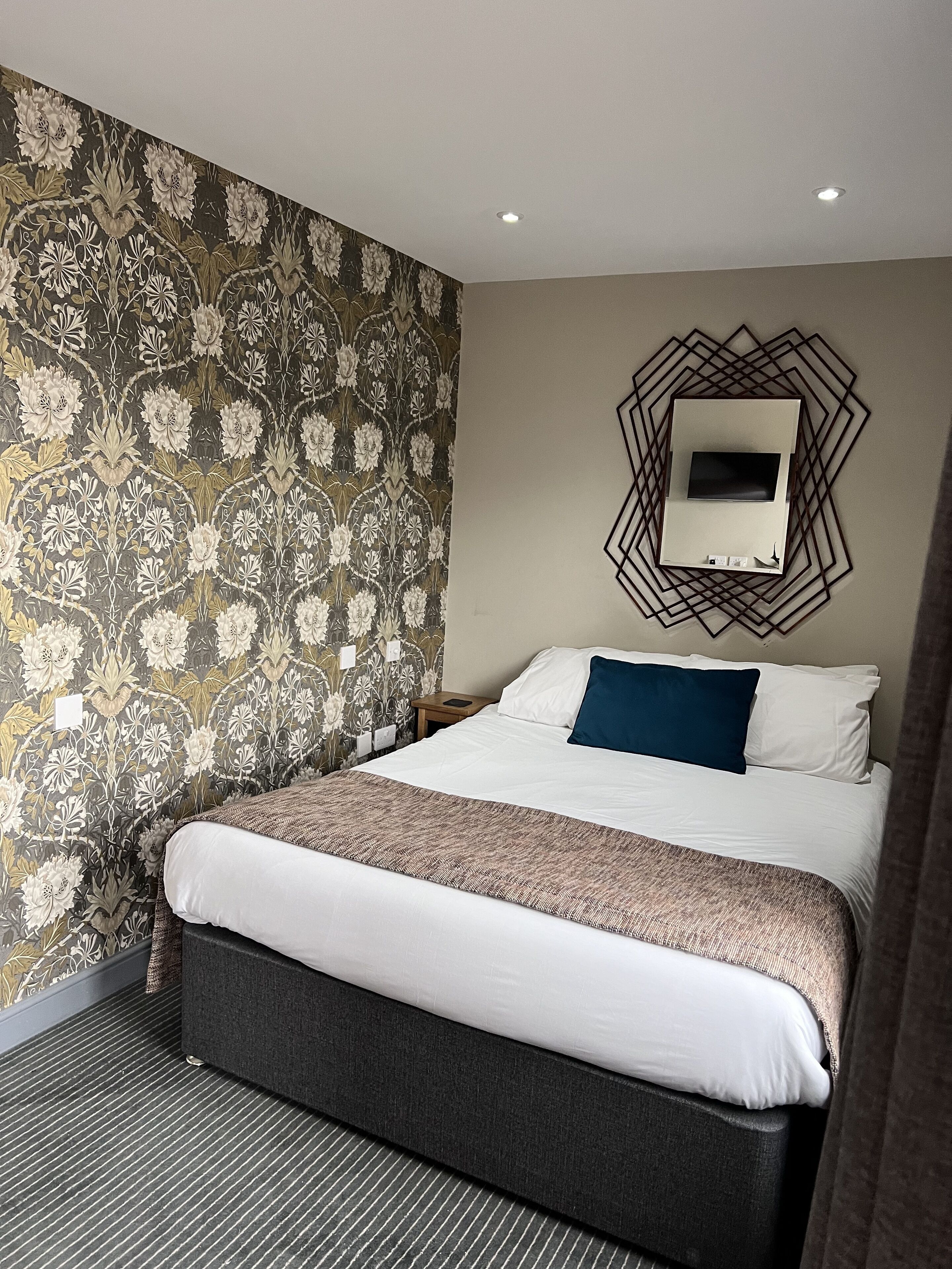 Ein Hotelzimmer mit einem großen Bett, einem Wand-Fernseher und einer Wandtapete mit Muster.