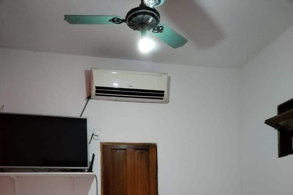 A small, compact room with a single bed, a TV on a shelf, and a ceiling fan.