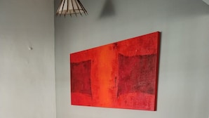 A room with a yellow sofa against a white wall, a red abstract painting above it, and a hanging light fixture. - Pousada Raysol Arraial d'Ajuda (Porto Seguro)