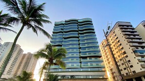 Un edificio moderno e slanciato, con numerosi balconi, circondato da palme e altri edifici.