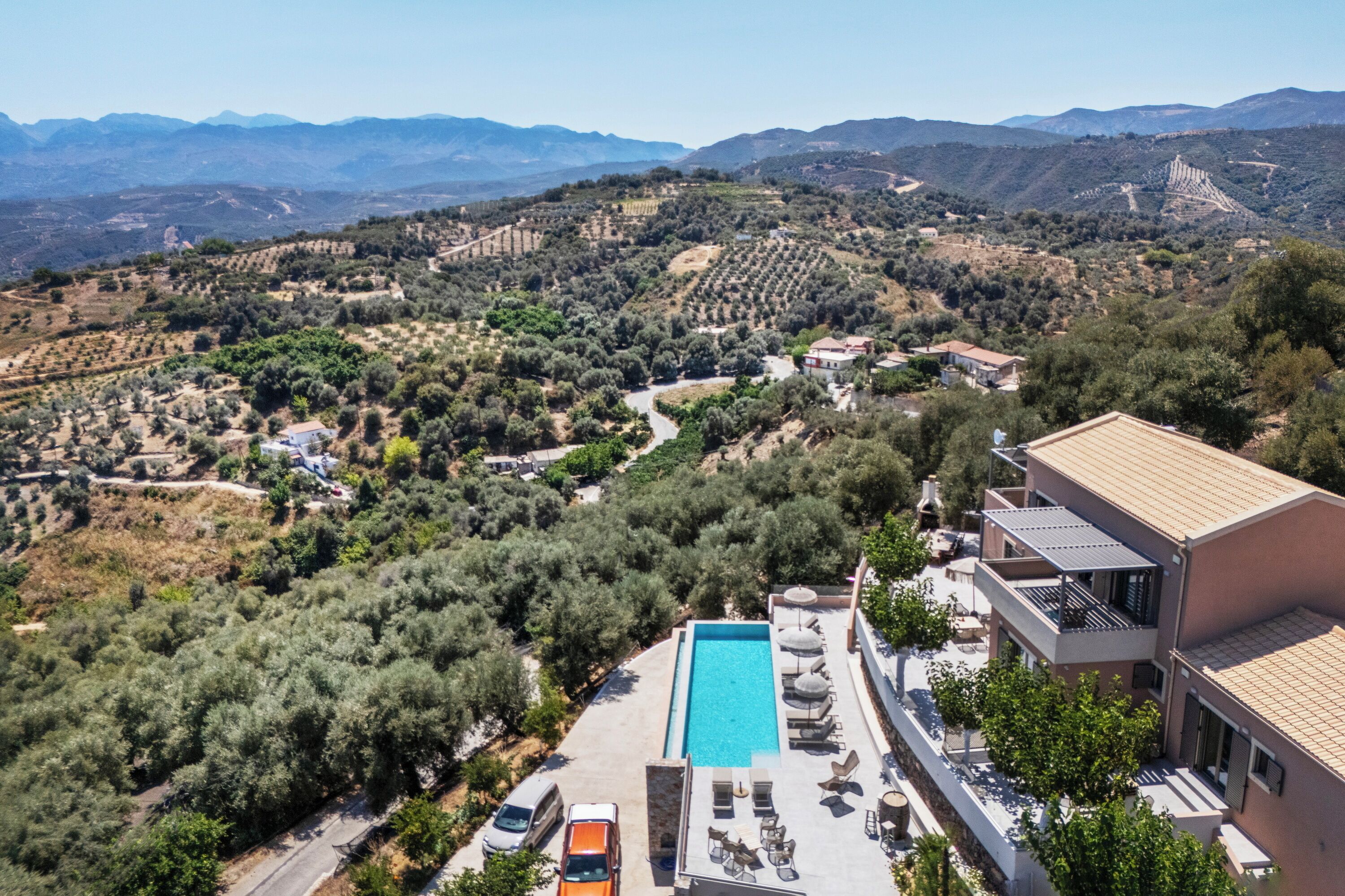 A modern hotel with a swimming pool, outdoor seating, and a view of the surrounding countryside.