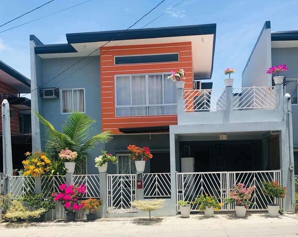 A modern two-story house with a garage, surrounded by a white fence and various potted plants.