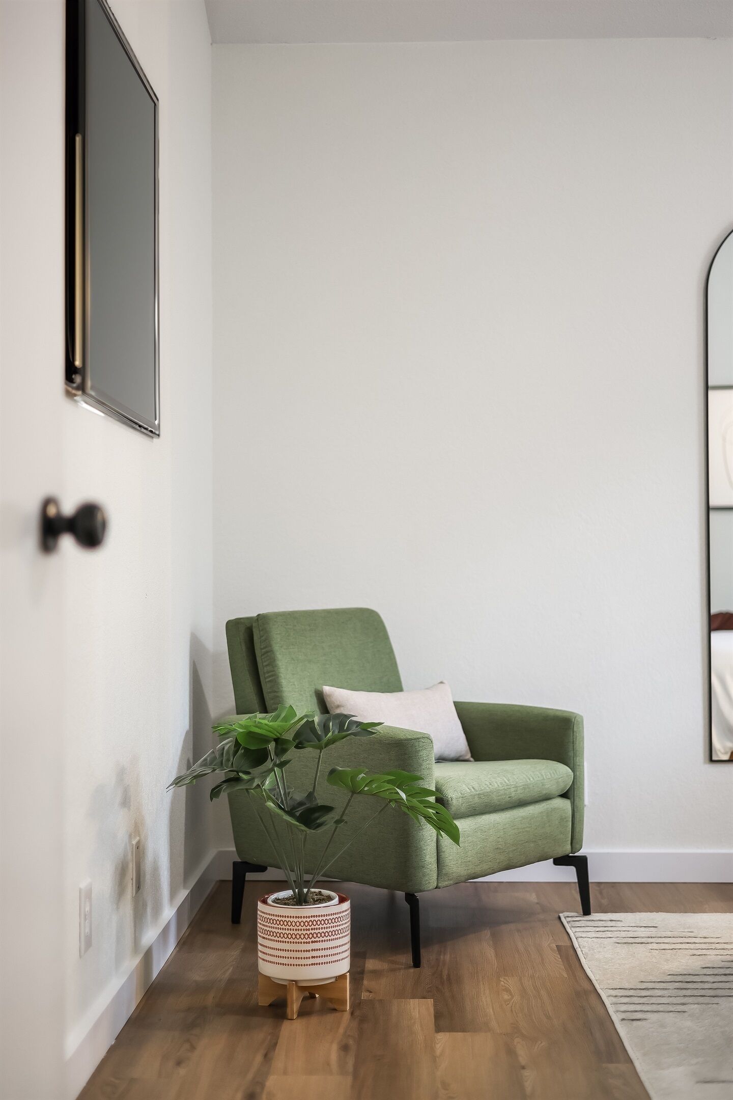 A green armchair with a plant beside it, a wooden floor, and a white wall with a door.