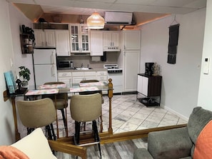 Una cocina funcional con armarios blancos, una mesa de comedor con sillas y una lámpara colgante.