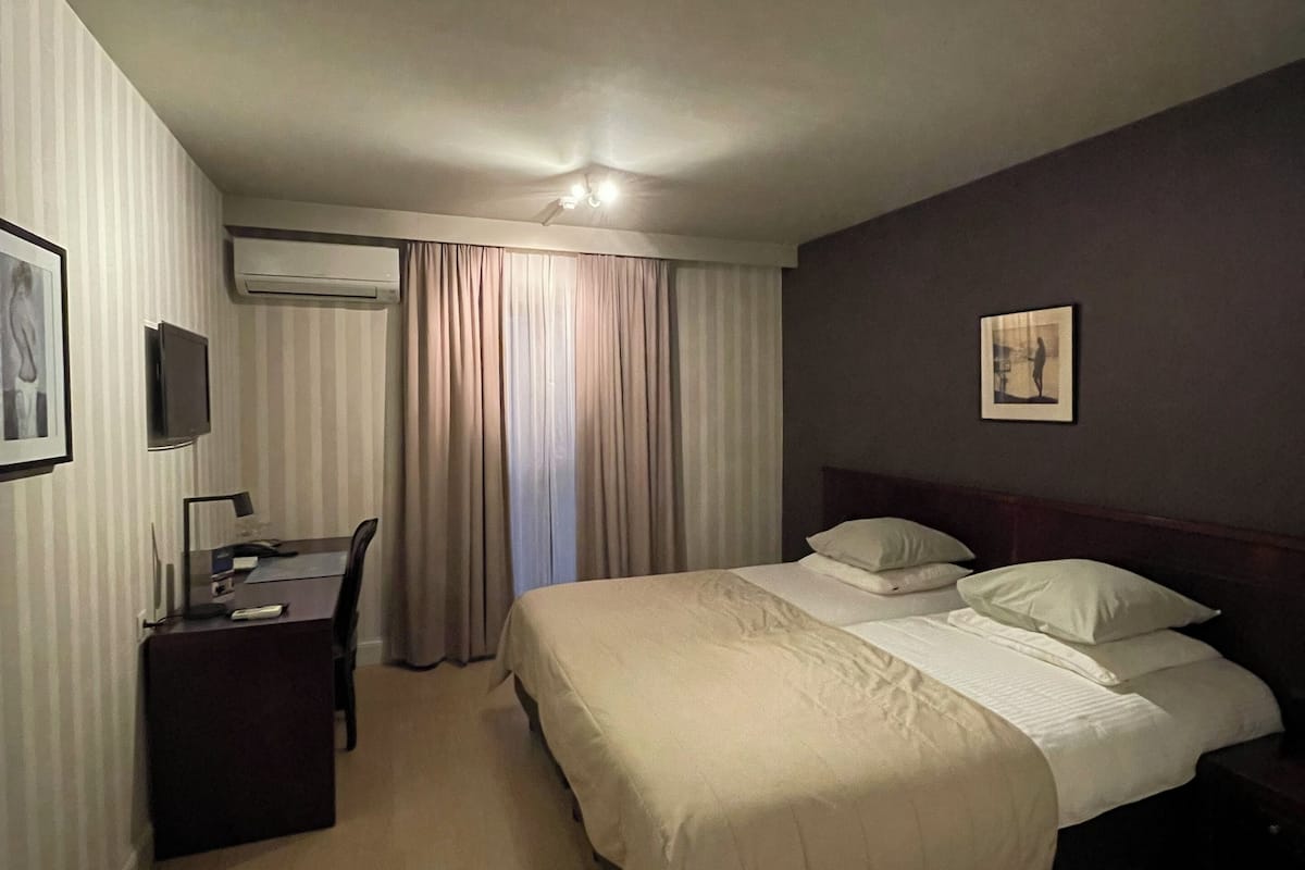 A hotel room with a bed, a desk, and an air conditioning unit.