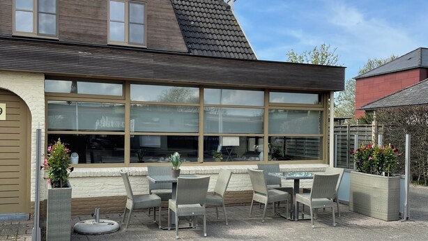 A hotel with a large sign, outdoor seating area with chairs and tables, and a view of the sky. - Hotel Prelude (Aalter)