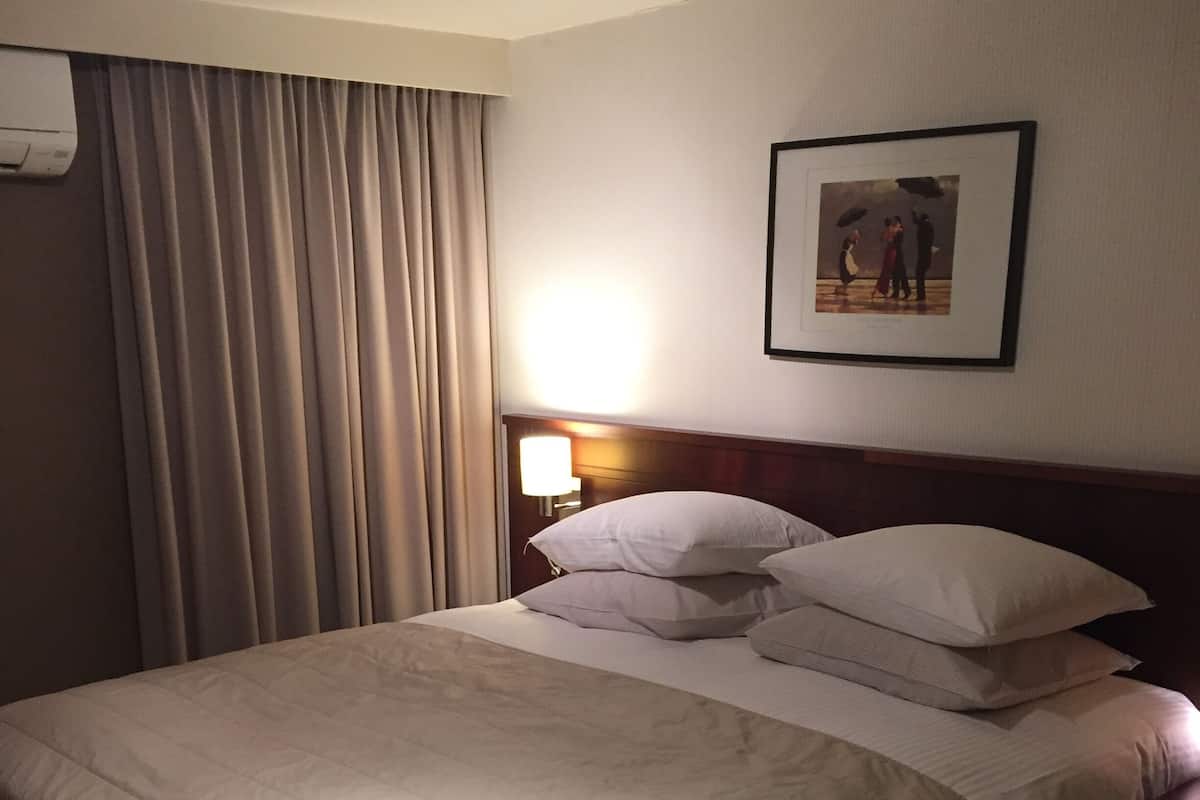 A hotel room with a large bed, a nightstand with a lamp, and a framed picture on the wall.