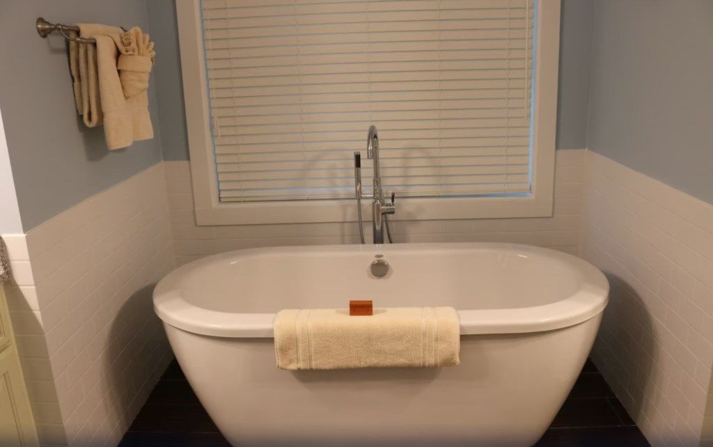 A bathroom with a freestanding bathtub, a window with blinds, and a towel rack with towels.